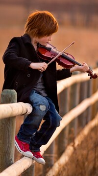 Chłopiec siedzący na ogrodzeniu i grający na skrzypcach