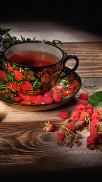 Maliny obok kolorowej filiżanki z herbatą