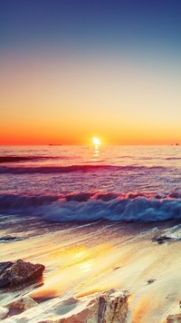 Morskie fale na kamienistej plaży o zachodzie słońca