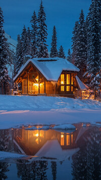 Oświetlony dom nad jeziorem w zimowej scenerii