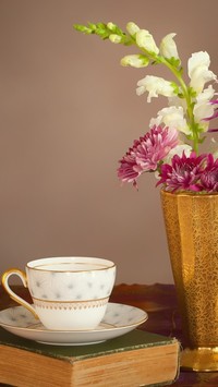 Pusta filiżanka obok wazonu z kwiatami i książka