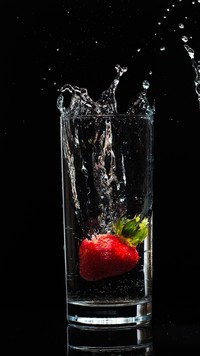 Truskawka wpadająca do szklanki z wodą