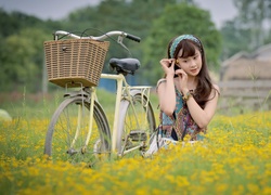 Azjatka obok roweru wśród żółtych kwiatów