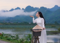 Azjatka w białej sukni z rowerem nad górską rzeką