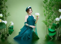 Azjatka w zielonej sukni z kwiatem lotosu w wodzie