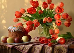 Babka i kolorowe jajka obok wazonu z czerwonymi tulipanami