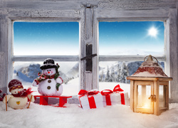 Bałwanki i prezenty obok lampionu na świątecznie udekorowanym oknie