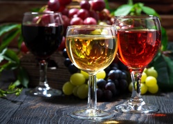 Białe i czerwone wino w kieliszkach obok kiści winogron