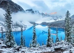 Błękitne jezioro otoczone ośnieżonymi drzewami w zamglonych górach