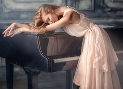 Blondynka w jasnoróżowej sukience oparta o fortepian