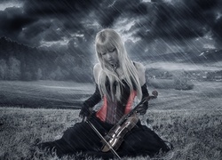 Blondynka ze skrzypcami siedzi na polu podczas deszczowej ulewy