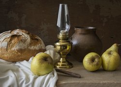 Bochenek chleba obok jabłek i lampy naftowej