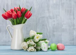 Bukiet czerwonych tulipanów w dzbanku obok białych tulipanów i pisanek