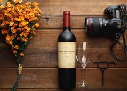 Butelka z winem i kieliszek obok aparatu fotograficznego i bukietu kwiatów
