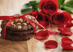 Ciasteczka przewiązane wstążką obok czerwonych róż