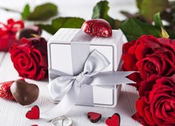 Czerwone róże i czekoladki obok prezentu