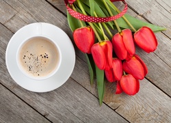 Czerwone tulipany położone na deskach obok filiżanki z kawą
