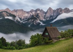 Dom na wzgórzu i mgła nad lasami w Alpach Julijskich