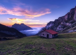 Dom na wzgórzu z widokiem na zamglone góry o zachodzie słońca