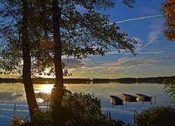 Drzewa i łódki na brzegu jeziora w blasku zachodzącego słońca