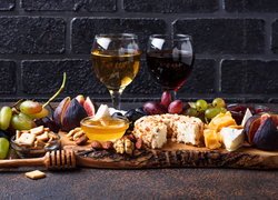 Dwa kieliszki z winem obok serów i owoców