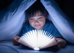 Dziecko pod kołdrą z rozświetloną książką