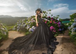 Dziewczyna w czarnej sukni obok kwiatów hortensji