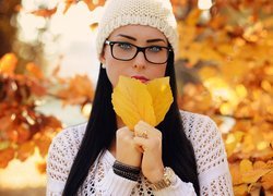 Dziewczyna w okularach i czapce trzyma liście w dłoniach