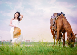 Dziewczyna w zwiewnej sukience na łące obok pasącego się konia