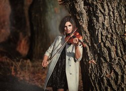 Dziewczyna ze skrzypcami oparta o drzewo
