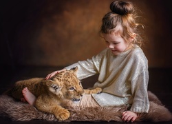 Dziewczynka głaszcze małe lwiątko