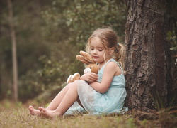 Dziewczynka siedzi pod drzewem w lesie przytulając pluszowego królika