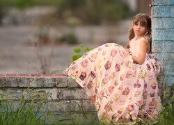 Dziewczynka w długiej sukience siedząca na murku