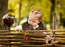 Dziewczynka z gałązką jarzębiny w rączce przy drewnianym ogrodzeniu