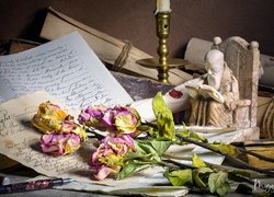 Figurka i świecznik obok uschniętych róż na listach