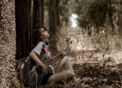 Grająca na gitarze dziewczyna siedzi pod drzewem