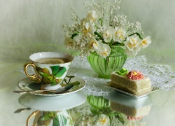 Herbata i ciasto na talerzyku obok wazonika z kwiatami