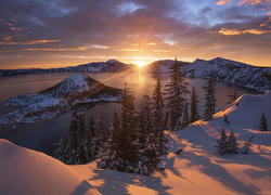 Jezioro otoczone zimowymi górami i drzewa w blasku zachodzącego słońca