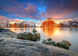 Kamienie przy brzegu jeziora z ośnieżonymi górami w tle o zachodzie słońca