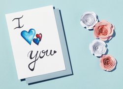 Kartka z wyznaniem miłosnym obok papierowych róż