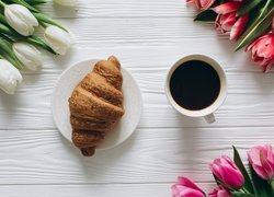 Kawa i croissant pośród tulipanów na deskach