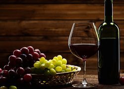 Kieliszek z winem obok butelki i winogron