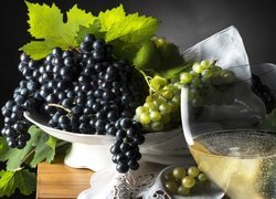 Kieliszek z winem obok kiści winogron na paterze