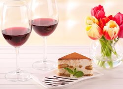 Kieliszki z winem obok ciasta i tulipanów w wazonie