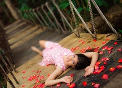 Kobieta leżąca na moście pośród rozsypanych płatków róż