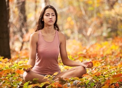 Kobieta siedząca na liściach w lesie podczas medytacji
