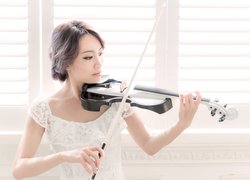 Kobieta w białej sukience grająca na skrzypcach