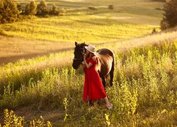 Kobieta w czerwonej sukience z koniem na łące