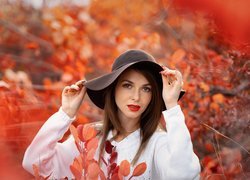 Kobieta w kapeluszu pośród czerwonych liści