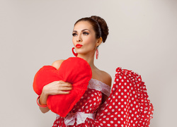 Kobieta w zwiewnej sukience przytula poduszkę w kształcie serca